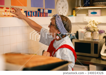 Caucasian senior woman reaching for storage boxes on a high shelf in a vibrant domestic kitchen Caucasian senior woman reaching for storage boxes on a high shelf in a vibrant domestic kitchen 140014326