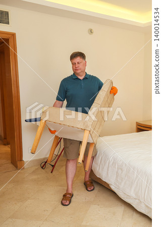 A man moves furniture to a new location in his spacious bedroom 140014534