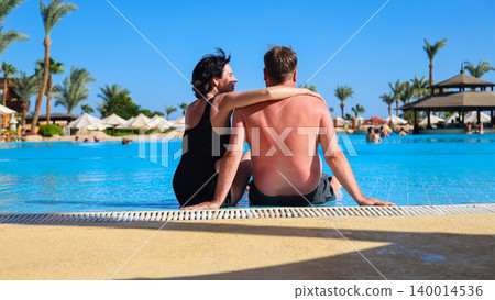 Husband and wife on vacation sitting near the pool, rear view Husband and wife on vacation sitting near the pool, rear view 140014536
