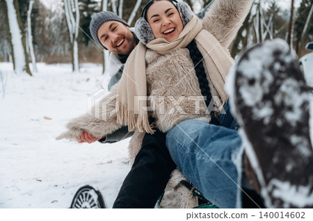 Joyful couple enjoying winter fun while sledding down snowy hill, surrounded by trees, capturing the essence of playful outdoor activities in a winter wonderland Joyful couple enjoying winter fun while sledding down snowy hill, surrounded by trees, capturing the essence of playful outdoor activities in a winter wonderland 140014602
