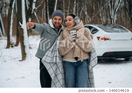Couple enjoying winter day in snowy forest, wrapped in blankets, smiling and taking photos with smartphone, capturing joyful moments in nature Couple enjoying winter day in snowy forest, wrapped in blankets, smiling and taking photos with smartphone, capturing joyful moments in nature 140014619
