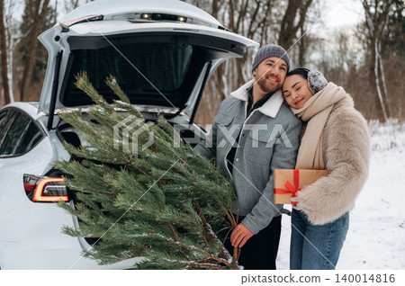Couple joyfully loading a Christmas tree into the back of a vehicle in a snowy forest, celebrating the holiday spirit with warmth and love Couple joyfully loading a Christmas tree into the back of a vehicle in a snowy forest, celebrating the holiday spirit with warmth and love 140014816