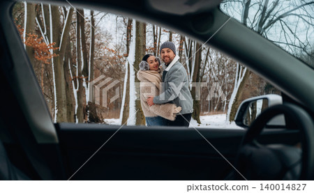 Couple embracing in winter landscape, surrounded by snow-covered trees, viewed through car window, capturing a moment of warmth and connection in a chilly environment Couple embracing in winter landscape, surrounded by snow-covered trees, viewed through car window, capturing a moment of warmth and connection in a chilly environment 140014827