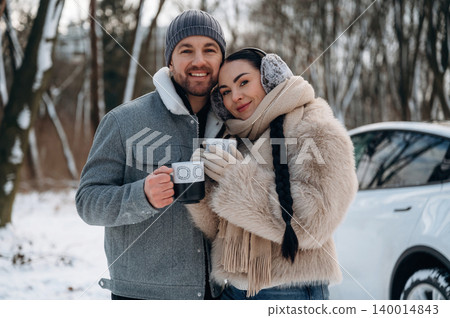 Couple enjoying warm beverages in winter attire, standing together in snowy landscape, showcasing love and warmth in a cold environment Couple enjoying warm beverages in winter attire, standing together in snowy landscape, showcasing love and warmth in a cold environment 140014843