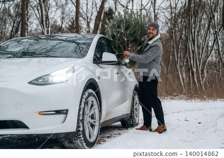 Man carrying Christmas tree beside electric vehicle in snowy forest, showcasing winter holiday spirit and outdoor adventure with festive atmosphere Man carrying Christmas tree beside electric vehicle in snowy forest, showcasing winter holiday spirit and outdoor adventure with festive atmosphere 140014862