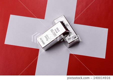 A silver bar, white metal against a backdrop of Swiss flag, as a concept for the sales. A silver bar A silver bar, white metal against a backdrop of Swiss flag, as a concept for the sales. A silver bar 140014916