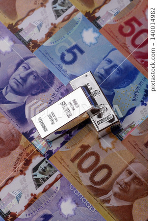 A silver bar, white metal against a backdrop of Canadian money, as a concept. A silver bar A silver bar, white metal against a backdrop of Canadian money, as a concept. A silver bar 140014982