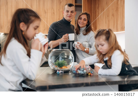 Family enjoying quality time together in a modern kitchen, with children engaged in activities and a fishbowl centerpiece enhancing the cozy atmosphere Family enjoying quality time together in a modern kitchen, with children engaged in activities and a fishbowl centerpiece enhancing the cozy atmosphere 140015017