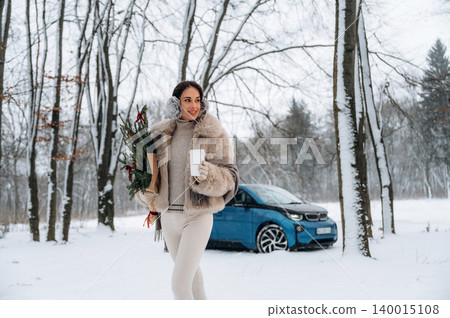 Woman in winter attire, holding flowers and a cup, walking through snowy forest landscape with trees, showcasing seasonal beauty and festive spirit in serene environment Woman in winter attire, holding flowers and a cup, walking through snowy forest landscape with trees, showcasing seasonal beauty and festive spirit in serene environment 140015108