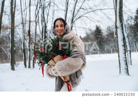 Smiling woman in winter attire holding festive greenery with red ribbons, surrounded by snow-covered trees, capturing the joy of the holiday season in a serene outdoor setting Smiling woman in winter attire holding festive greenery with red ribbons, surrounded by snow-covered trees, capturing the joy of the holiday season in a serene outdoor setting 140015150