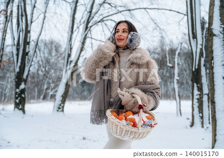 Woman in winter coat with fur accents, holding a basket of oranges, smiling while talking on the phone in a snowy forest, capturing the essence of winter joy and connection Woman in winter coat with fur accents, holding a basket of oranges, smiling while talking on the phone in a snowy forest, capturing the essence of winter joy and connection 140015170