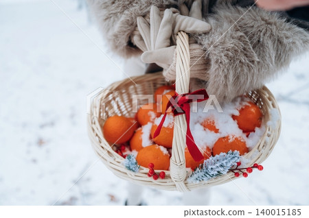 Woman in cozy winter attire holds a woven basket filled with bright oranges and snow, surrounded by a serene snowy landscape, evoking a festive holiday spirit Woman in cozy winter attire holds a woven basket filled with bright oranges and snow, surrounded by a serene snowy landscape, evoking a festive holiday spirit 140015185