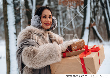 Woman in winter attire, wearing earmuffs, carries beautifully wrapped gifts in a snowy forest, showcasing festive spirit and holiday joy in a serene outdoor setting Woman in winter attire, wearing earmuffs, carries beautifully wrapped gifts in a snowy forest, showcasing festive spirit and holiday joy in a serene outdoor setting 140015198