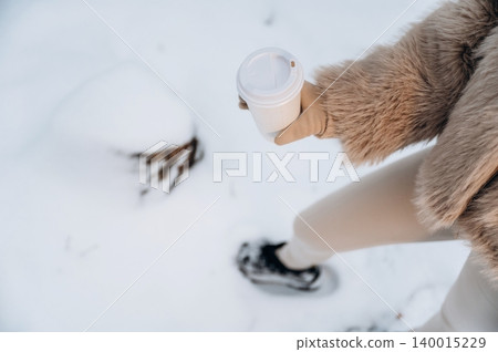 Woman in stylish fur coat holding coffee cup while walking through snowy landscape, showcasing winter fashion and cozy outdoor lifestyle in a serene environment Woman in stylish fur coat holding coffee cup while walking through snowy landscape, showcasing winter fashion and cozy outdoor lifestyle in a serene environment 140015229