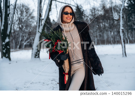 Stylish woman with sunglasses, dressed in cozy winter attire, holding a festive bouquet of greenery, walking through a snowy landscape, embracing the holiday spirit and winter charm Stylish woman with sunglasses, dressed in cozy winter attire, holding a festive bouquet of greenery, walking through a snowy landscape, embracing the holiday spirit and winter charm 140015296