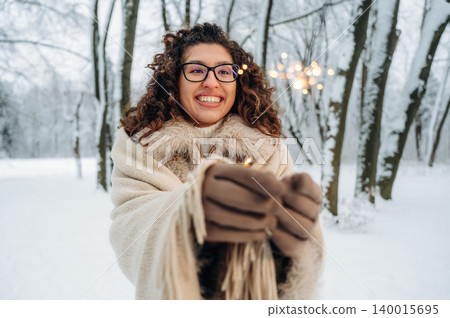 Smiling woman with curly hair, wearing warm clothing, holding sparklers in a snowy forest, surrounded by trees, celebrating winter festivities with joy and excitement Smiling woman with curly hair, wearing warm clothing, holding sparklers in a snowy forest, surrounded by trees, celebrating winter festivities with joy and excitement 140015695