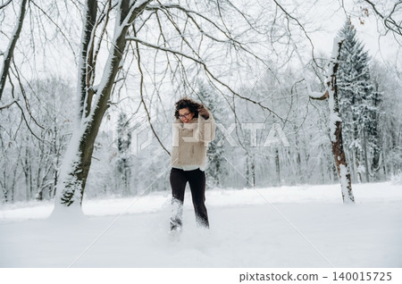 Young woman with curly hair in cozy sweater joyfully playing in fresh snow, surrounded by winter trees, capturing the essence of a playful winter day in a serene landscape Young woman with curly hair in cozy sweater joyfully playing in fresh snow, surrounded by winter trees, capturing the essence of a playful winter day in a serene landscape 140015725