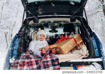 Young child with light brown hair, wearing winter clothing, sitting in the trunk of a car, surrounded by snow, holding a gift box, evoking holiday spirit and joy Young child with light brown hair, wearing winter clothing, sitting in the trunk of a car, surrounded by snow, holding a gift box, evoking holiday spirit and joy 140015740