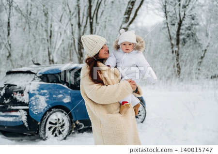 Woman in cozy winter coat holds child in snowy landscape near blue car, showcasing family bonding and joy during winter activities in a serene environment Woman in cozy winter coat holds child in snowy landscape near blue car, showcasing family bonding and joy during winter activities in a serene environment 140015747