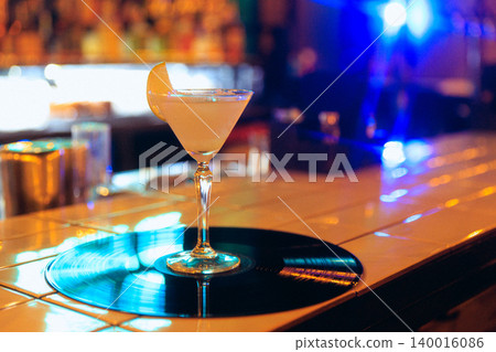 Orange coupe cocktail on vinyl record with bright blue neon bar background. Orange coupe cocktail on vinyl record with bright blue neon bar background. 140016086