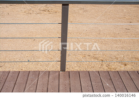 Fragment of a modern cable railing on a beach wooden terrace deck. Fragment of a modern cable railing on a beach wooden terrace deck. 140016146