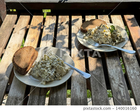 Meat and Potato Salad with Rye Bread Slice on Sunny Wooden Table. Meat and Potato Salad with Rye Bread Slice on Sunny Wooden Table. 140016160