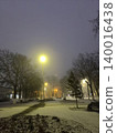 A peaceful winter night in a park, with snow covering the ground and warm street lamps casting soft shadows. The serene atmosphere invites quiet contemplation and leisurely strolls. 140016438