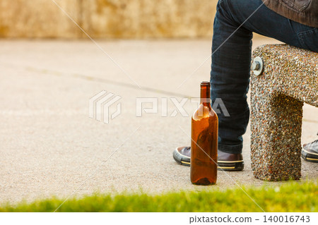 Man depressed with wine bottle sitting on bench outdoor 140016743