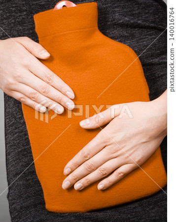 Girl having stomach ache, holding hot water bottle 140016764