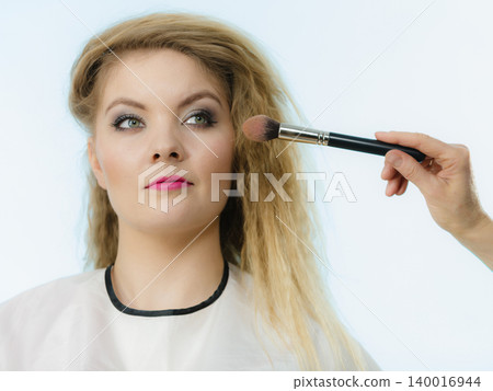 Makeup artist applying with brush rouge on female check Makeup artist applying with brush rouge on female check 140016944