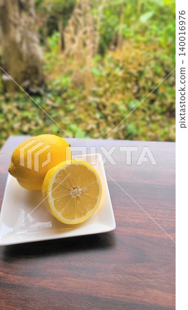 在翠綠的背景下,鮮亮的檸檬(整顆和切片)擺放在白色盤子上。 在翠綠的背景下,鮮亮的檸檬(整顆和切片)擺放在白色盤子上。 140016976