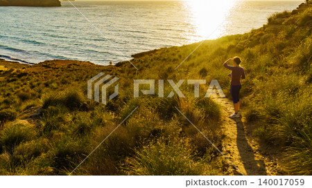 Woman stands on cliff overlooking sea at sunrise Woman stands on cliff overlooking sea at sunrise 140017059