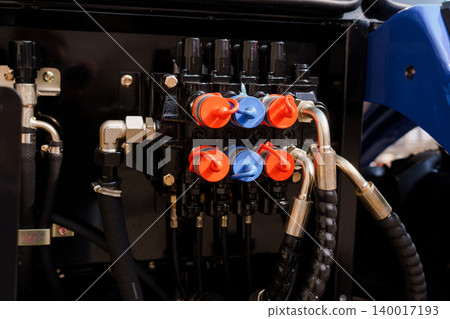 Close up of hydraulic control valve manifold with red and blue caps on heavy machinery equipment Close up of hydraulic control valve manifold with red and blue caps on heavy machinery equipment 140017193