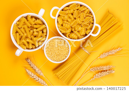 Assorted dry pasta types with wheat ears on yellow background Assorted dry pasta types with wheat ears on yellow background 140017225
