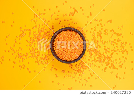 Red lentils filling bowl on vibrant yellow background Red lentils filling bowl on vibrant yellow background 140017230