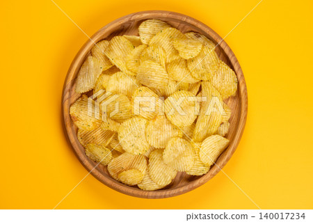 Wavy potato chips filling a wooden bowl Wavy potato chips filling a wooden bowl 140017234