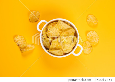 Crispy ruffled potato chips in bowl on yellow background 140017235