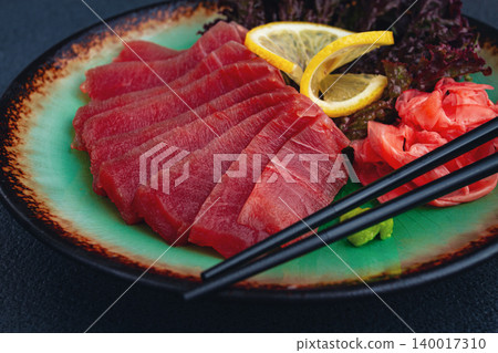 Fresh tuna sashimi served with lemon, wasabi, and pickled ginger on a dark background Fresh tuna sashimi served with lemon, wasabi, and pickled ginger on a dark background 140017310