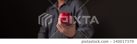 Man hand holding red heart shape on dark background. Concept of love, healthcare, medical insurance and charity donation. Valentine's day symbol for romantic relationship and kindness support. Man hand holding red heart shape on dark background. Concept of love, healthcare, medical insurance and charity donation. Valentine's day symbol for romantic relationship and kindness support. 140017379