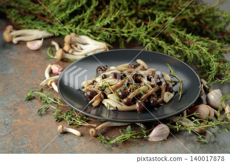Fried shimeji mushrooms with thyme and garlic on a black plate. Fried shimeji mushrooms with thyme and garlic on a black plate. 140017878