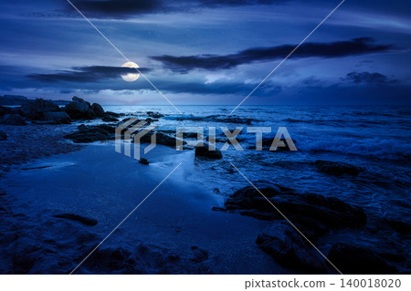 huge stones on a sandy beach at night. wonderful summer vacation season at the black sea. full moon over calm waves washing the sand shore. mysterious nature background with cloudy sky huge stones on a sandy beach at night. wonderful summer vacation season at the black sea. full moon over calm waves washing the sand shore. mysterious nature background with cloudy sky 140018020