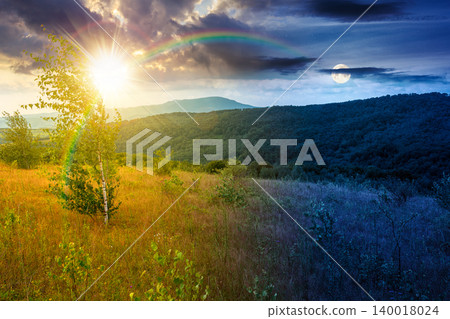 tree on a field in mountain landscape. day meet night. sun and moon over green countryside of ukraine in summer. cloudy weather. carpathian landscape in dappled light. amazing carpathian highland tree on a field in mountain landscape. day meet night. sun and moon over green countryside of ukraine in summer. cloudy weather. carpathian landscape in dappled light. amazing carpathian highland 140018024