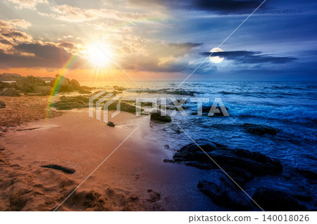huge stones on a sandy beach. day meet night. epic summer vacation season at the black sea. sun and moon in harmony over calm waves washing the sand shore. nature background with cloudy sky huge stones on a sandy beach. day meet night. epic summer vacation season at the black sea. sun and moon in harmony over calm waves washing the sand shore. nature background with cloudy sky 140018026
