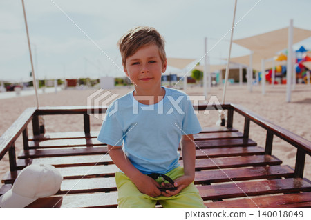 Portrait of boy sitting on swing on the beach at summer Portrait of boy sitting on swing on the beach at summer 140018049
