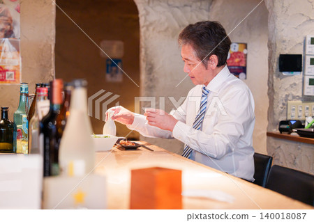 一位老人獨自坐在居酒屋(日本酒吧)的吧台旁。 一位老人獨自坐在居酒屋(日本酒吧)的吧台旁。 140018087