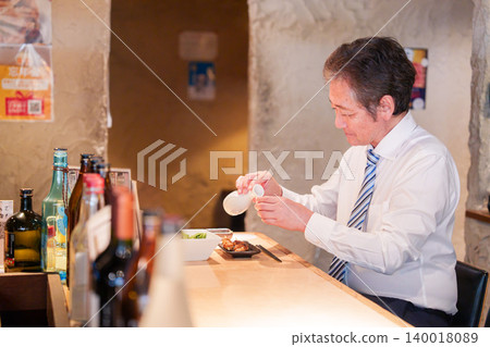 一位老人獨自坐在居酒屋(日本酒吧)的吧台旁。 一位老人獨自坐在居酒屋(日本酒吧)的吧台旁。 140018089