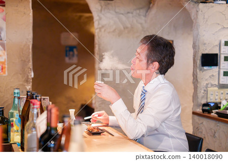 一位老人獨自坐在居酒屋（日本酒吧）的吧台旁。 140018090