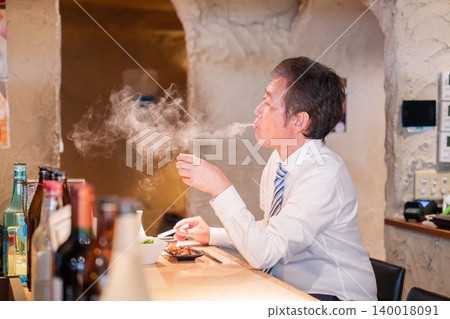一位老人獨自坐在居酒屋(日本酒吧)的吧台旁。 一位老人獨自坐在居酒屋(日本酒吧)的吧台旁。 140018091