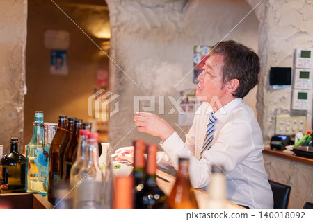An elderly man sitting alone at the counter in an izakaya (Japanese pub). An elderly man sitting alone at the counter in an izakaya (Japanese pub). 140018092