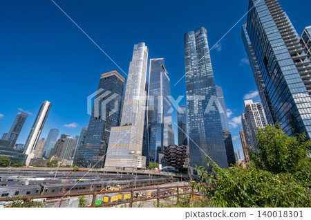 New york, usa august 20,2024. Hudson yards complex showcasing numerous contemporary skyscrapers and the vessel structure against a clear blue sky, with train yards below New york, usa august 20,2024. Hudson yards complex showcasing numerous contemporary skyscrapers and the vessel structure against a clear blue sky, with train yards below 140018301